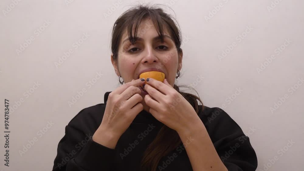 A woman having a healthy snack. Closeup view of a latin american woman eating an orange slice with a white background A woman having a healthy snack. Closeup view of a latin american woman eating an orange slice with a white background