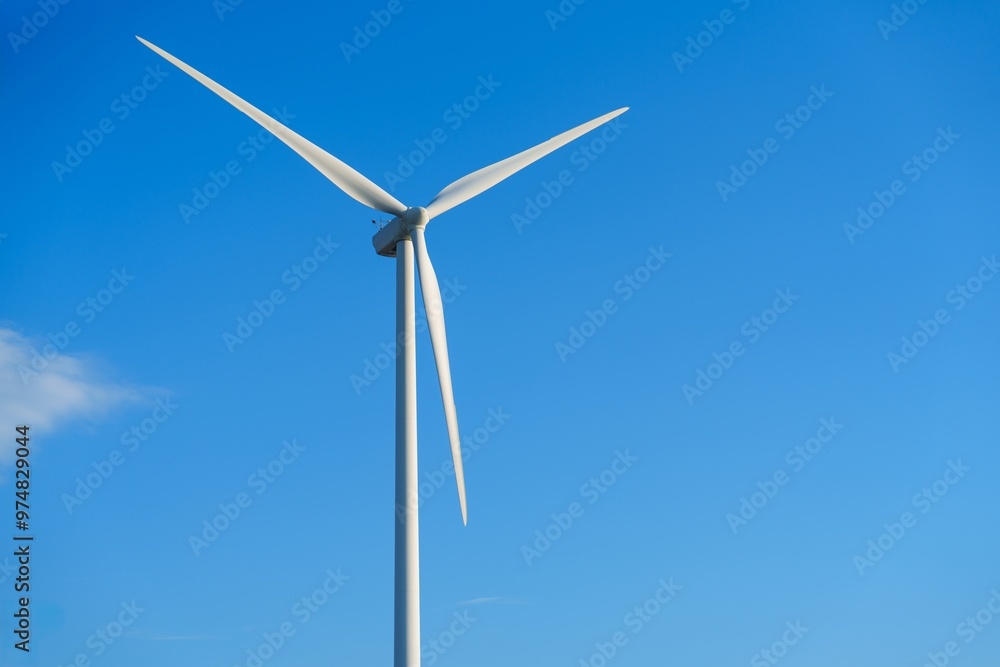 A lone white windmill stands tall against a clear blue sky, symbolizing the beauty of renewable energy. This wind turbine represents an eco-friendly source of power, contributing to a sustainable A lone white windmill stands tall against a clear blue sky, symbolizing the beauty of renewable energy. This wind turbine represents an eco-friendly source of power, contributing to a sustainable