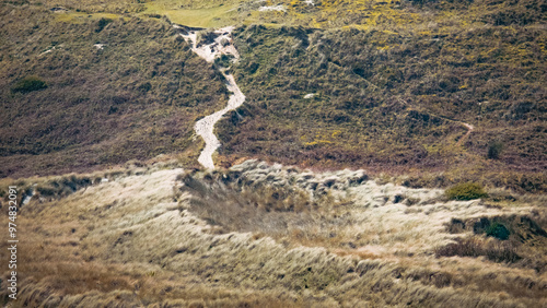 A winding dirt path through grassy hills on a sunny day in a tranquil rural landscape. photo