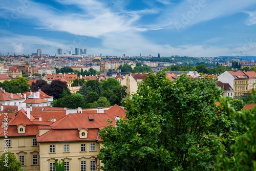 Stunning view of a charming cityscape featuring an array of red-roofed buildings, enveloped by the vibrant green of lush trees, all set against a captivating blue sky dotted with fluffy white clouds. photo