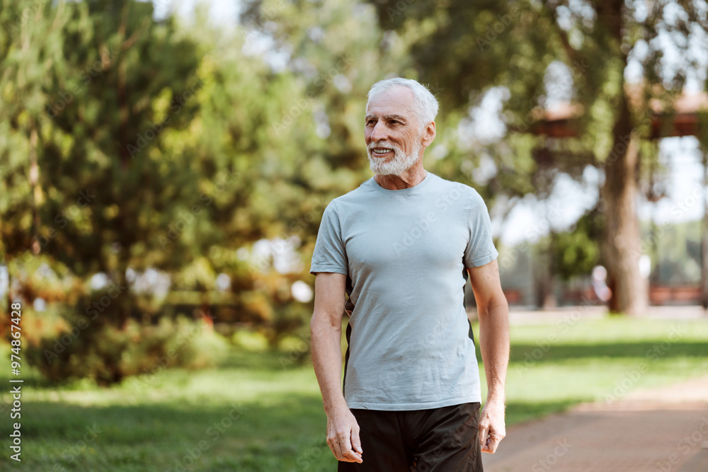 Attractive, smiling elderly man wearing t shirt enjoying sunny walk in park, looking away Attractive, smiling elderly man wearing t shirt enjoying sunny walk in park, looking away