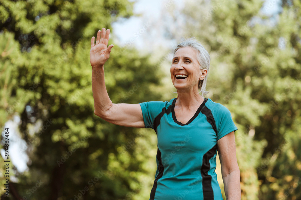 Happy senior woman waving hand while exercising in park, looking away Happy senior woman waving hand while exercising in park, looking away