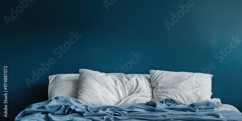 Cozy bed with white pillows and blue blanket against a dark blue wall, creating a serene and inviting atmosphere. photo