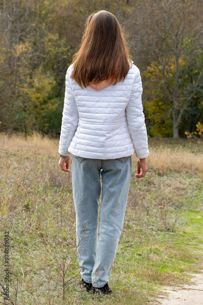 Young woman look on autumn landscape. She see beautiful fall with yellow and red leaves. Girl in white jacket and with long brown hair walks along meadow path. Beautiful trees and nature of autumn. Young woman look on autumn landscape. She see beautiful fall with yellow and red leaves. Girl in white jacket and with long brown hair walks along meadow path. Beautiful trees and nature of autumn.