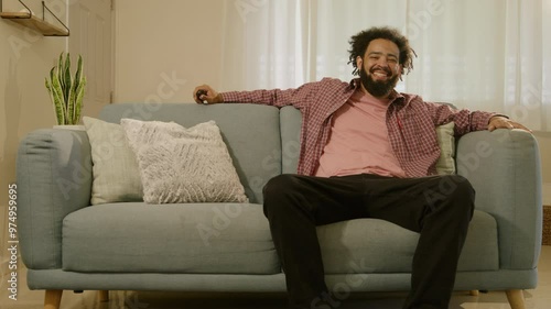 A smiling young man is casually sitting on a comfortable sofa, holding his mobile phone while browsing the internet and enjoying a welldeserved moment of relaxation and leisure in his home photo