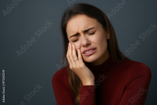 A beautiful young woman is visibly distressed, touching her cheek in pain due to severe toothache. She appears to be in a moment of discomfort while considering dental care options