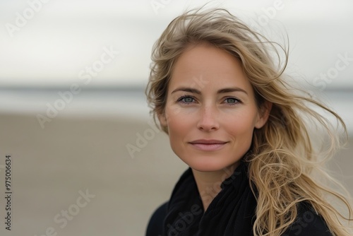 Portrait of a blonde middle-aged woman with windblown hair standing on the beach in natural lighting.