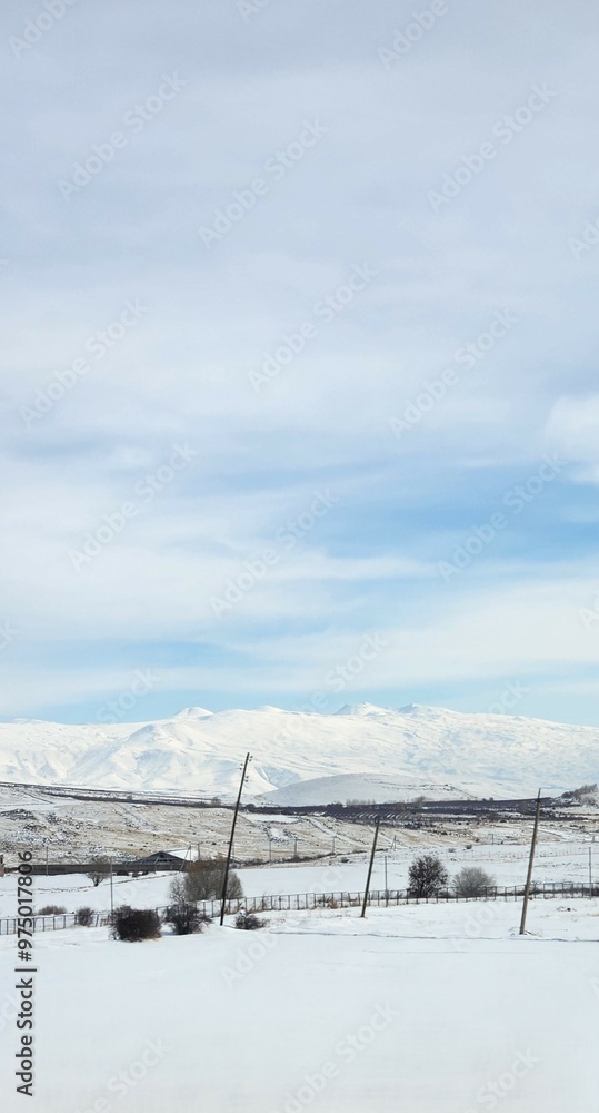 A winter landscape with endless white fields stretching toward distant snow-covered mountains. The pale blue sky meets the horizon, where the soft contours of the mountains blend with the wintry scene A winter landscape with endless white fields stretching toward distant snow-covered mountains. The pale blue sky meets the horizon, where the soft contours of the mountains blend with the wintry scene