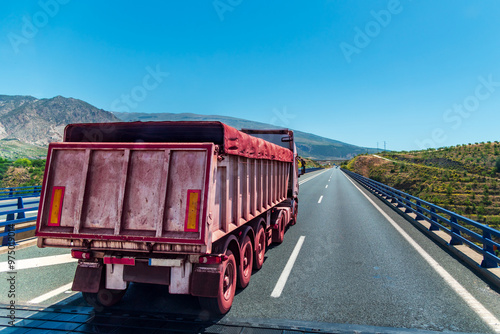 Truck with a tipper trailer travelling on a motorway transporting iron ore, the truck is covered in a reddish colour due to its entry into iron ore quarries.