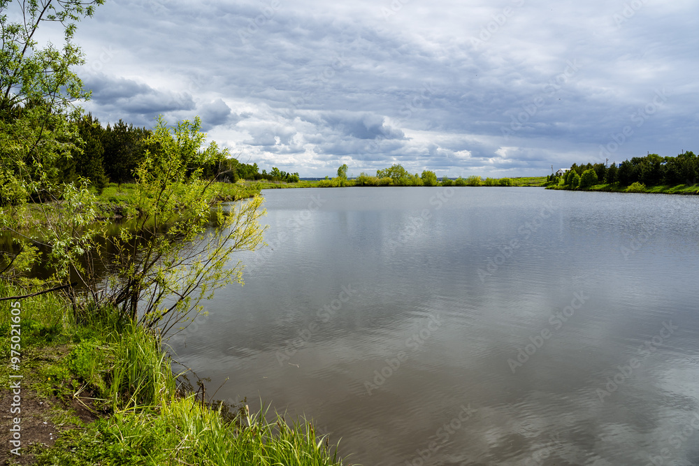 A large body of water surrounded entirely by green trees on a cloudy day A large body of water surrounded entirely by green trees on a cloudy day