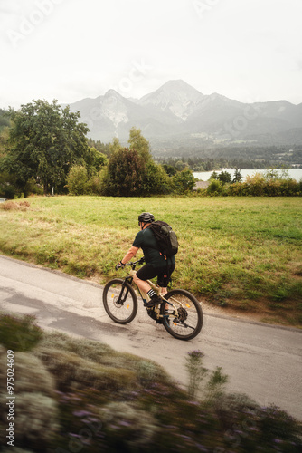 Mann fährt mit Fahrrad am Egger Marterl mit Blick auf den Faaker See und die Berge dahinter in Villach in Kärnten Österreich photo