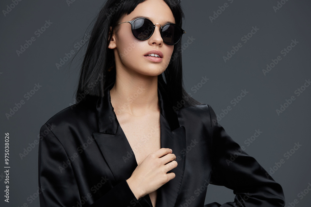 Woman in black suit and sunglasses, posing confidently with hands on hips against a gray background, expressing power and elegance Woman in black suit and sunglasses, posing confidently with hands on hips against a gray background, expressing power and elegance