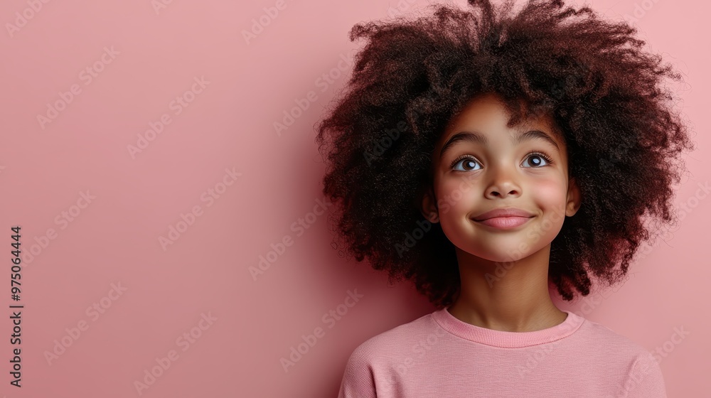 A young girl with curly hair looks upwards smiling. Her pink shirt matches the solid pink background, adding to her joyful childlike innocence. A young girl with curly hair looks upwards smiling. Her pink shirt matches the solid pink background, adding to her joyful childlike innocence.