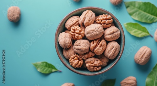 Healthy walnuts in a decorative bowl surrounded by leaves on a vibrant blue s...