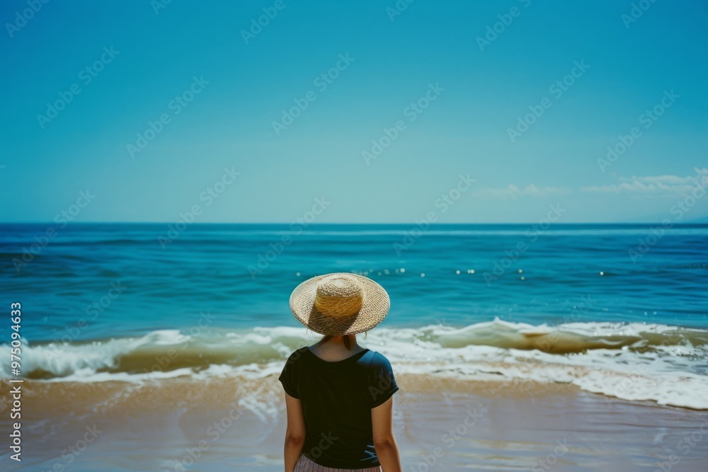Φωτογραφία A person in a white dress and straw hat stands facing the endless ocean, under a bright blue sky dotted with fluffy clouds, capturing a moment of serene contemplation