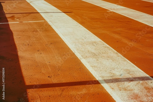 A close-up of a red race track with white lines prominently marking the lanes, bathed in warm sunlight, evoking a sense of competition and athleticism.