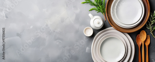 Elegant white plates and wooden utensils neatly arranged on a gray textured surface with rosemary sprigs, minimalist kitchen setup.
