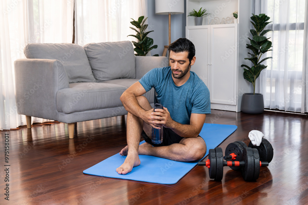 Athletic and sporty man drinking water on fitness mat after finishing home body workout exercise session for fit physique and healthy sport lifestyle at home. Gaiety home exercise workout training. Athletic and sporty man drinking water on fitness mat after finishing home body workout exercise session for fit physique and healthy sport lifestyle at home. Gaiety home exercise workout training.