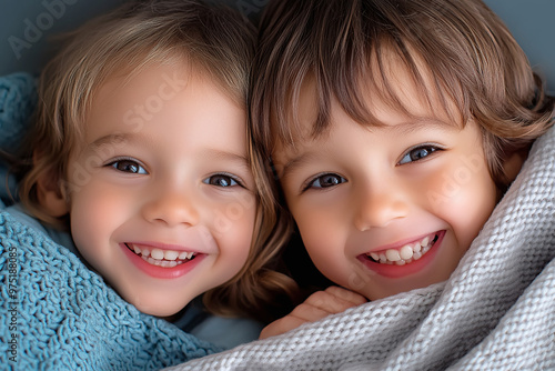 two happy preschool kids are smiling in the camera with a blanket around them