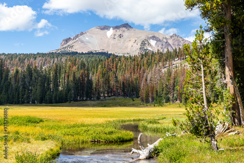 Lassen Peak and Kings Creek - A scenic landscape features a clear stream flowing through a verdant meadow, with lush pine forests leading up to rugged mountains in the background.