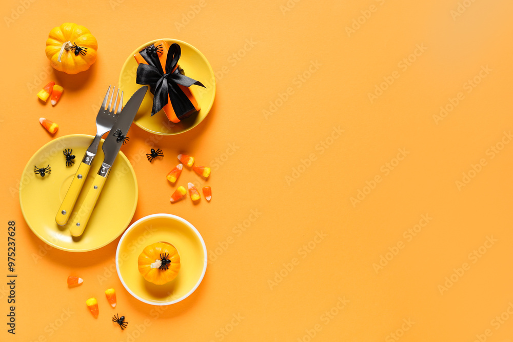 Festive table setting for Halloween celebration with gift box, candies and pumpkins on orange background Festive table setting for Halloween celebration with gift box, candies and pumpkins on orange background