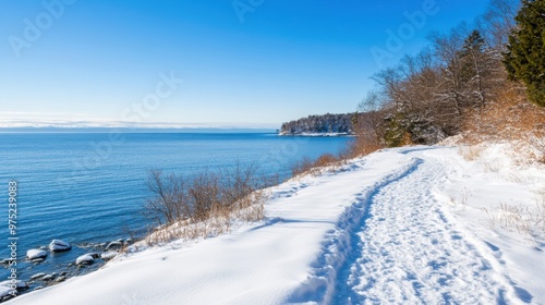 A tranquil path blanketed in snow runs beside the calm sea, beckoning walkers to enjoy the bright winter day