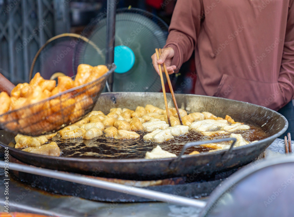 A vendor uses chopsticks to flip the deep-fried dough stick. A vendor uses chopsticks to flip the deep-fried dough stick.