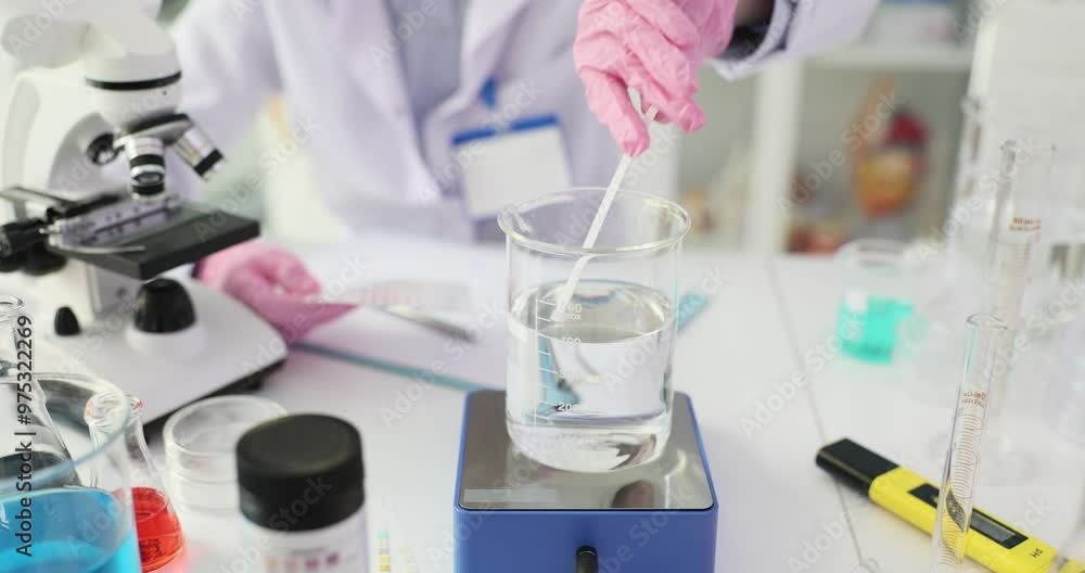 Scientist analyzes water sample using PH test strips in laboratory. Chemist compares color pattern on paper with table at workplace Scientist analyzes water sample using PH test strips in laboratory. Chemist compares color pattern on paper with table at workplace