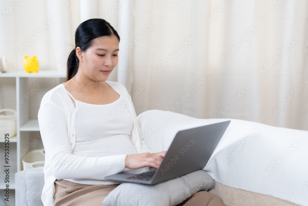 Asian pregnant woman sitting on sofa using laptop, smiling softly, showing a sense of joy and care. Warm, cozy room with soft furnishings, creating an atmosphere of comfort and maternal love. Asian pregnant woman sitting on sofa using laptop, smiling softly, showing a sense of joy and care. Warm, cozy room with soft furnishings, creating an atmosphere of comfort and maternal love.