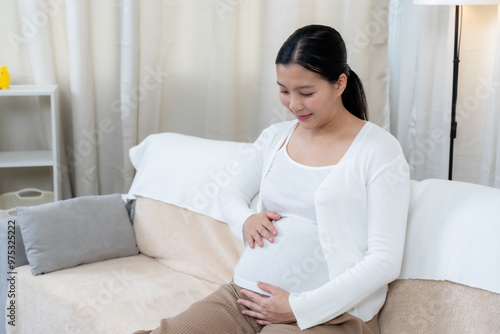 Asian pregnant woman relaxing on sofa with calm expression, hands resting on belly, conveying peacefulness and bond with unborn baby. Soft natural lighting adds warmth, creating nurturing environment Free Download Asian pregnant woman relaxing on sofa with calm expression, hands resting on belly, conveying peacefulness and bond with unborn baby. Soft natural lighting adds warmth, creating nurturing environment - GFXLoad