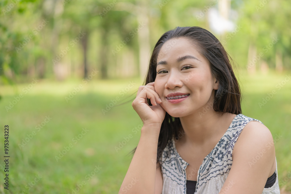 Happy young woman sitting looking at camera looking cheerful and relaxed in a quiet environment in the middle of a garden. Summer time. Spending time in nature. Maintaining a healthy lifestyle Happy young woman sitting looking at camera looking cheerful and relaxed in a quiet environment in the middle of a garden. Summer time. Spending time in nature. Maintaining a healthy lifestyle