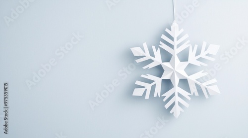 White paper snowflake hanging on pale blue background