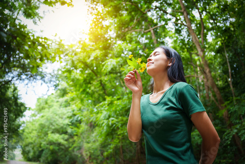 A cheerful young asian woman enjoys a sunny day outdoors, holding a vibrant bunch of yellow flowers. Smiling in a green field, she embodies the joy and freedom of summer in the countryside.