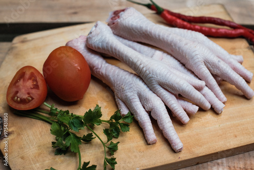 Fresh raw chicken feet on a wooden cutting board, with ingredients typically used in cooking, preparation for a dish that incorporates these ingredients.