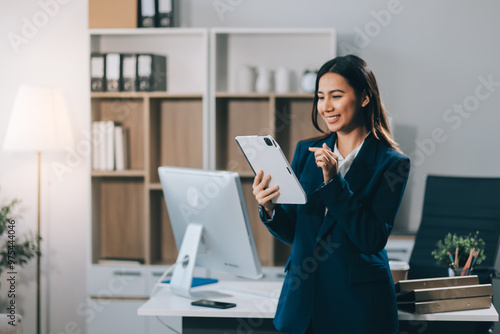 Young smart businesswoman holding digital tablet while holding coffee cup and standing in the modern office room.