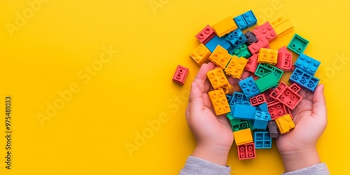 Hand holding colorful plastic brick toys, blocks for building toys on yellow background, with space area for text photo