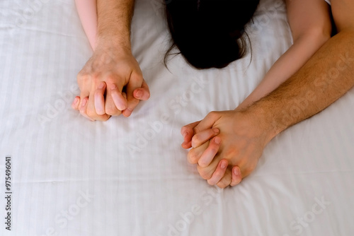 Man is stroking woman's hands lying in bed with white linen making love, hands close-up. Sex, intimate life, pleasure and love concept. Two lovers having a sex holding hands, sensual gesture.