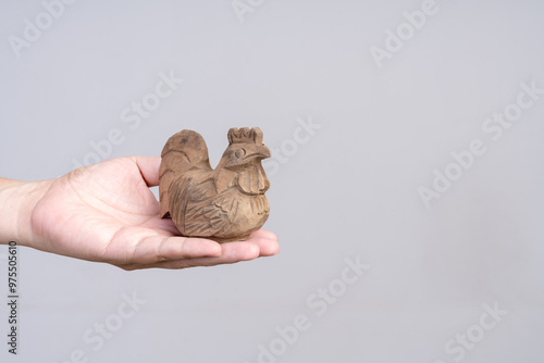 Hand holding a carved wooden rooster figurine against a plain background.