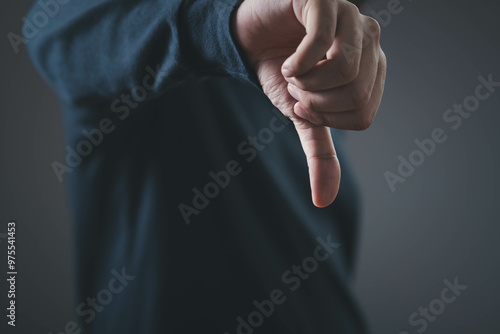 Close-up of a hand showing a thumbs down gesture against a dark background, representing disapproval or negativity. photo