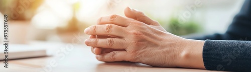 Close-up of a person clasping their hands on a desk, conveying contemplation or conversation in a professional setting.
