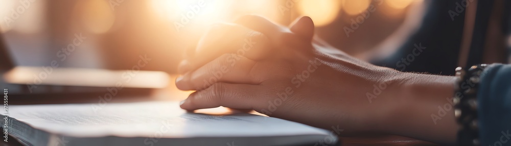 Close-up of hands resting on an open book with sunlight in the background, depicting calm and focus during study or work. Close-up of hands resting on an open book with sunlight in the background, depicting calm and focus during study or work.