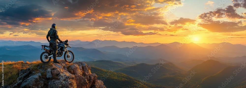 Obraz premium A man is riding a motorcycle on a mountain top at sunset. The sky is filled with clouds and the sun is setting, creating a beautiful and serene atmosphere