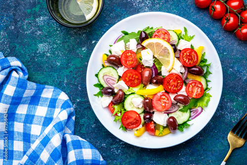 Greek salad with feta cheese, olives, tomatoes, lettuce, paprika, cucumber and onion. Blue background, top view