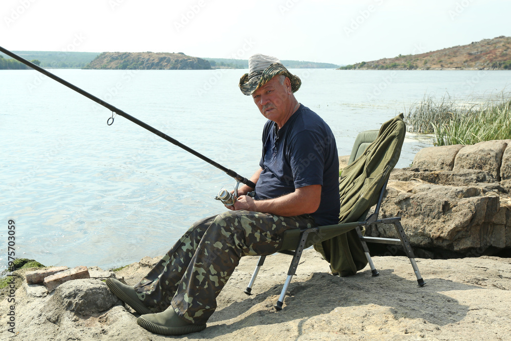 Fisherman with rod sitting on chair and fishing near lake at summer Fisherman with rod sitting on chair and fishing near lake at summer