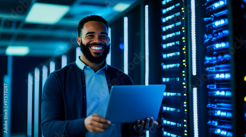 Wallpaper Mural A cheerful engineer is standing in a brightly lit data center, surrounded by towering server racks filled with glowing equipment. He is smiling while working on a laptop, configuri Torontodigital.ca