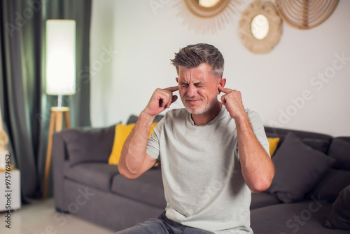 Man covering his ears, stressed or unhappy because of loud music or too much noise. Indoors shot