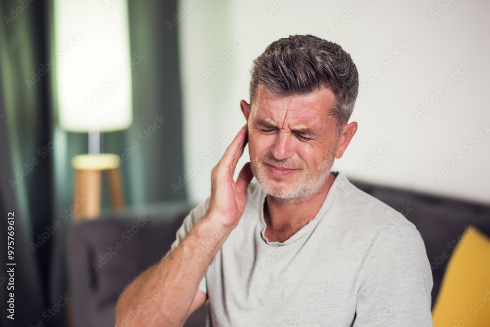 Man suffering for ear pain sitting in the room, close up Man suffering for ear pain sitting in the room, close up