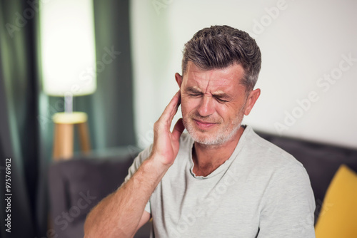 Man suffering for ear pain sitting in the room, close up photo