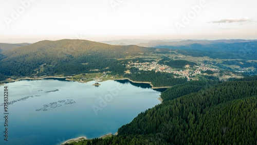 Lake and mountains surrounded by forests in the colorful rays of the setting sun in Bulgaria. Fish farms trout and other fish on the lake. Aerial shot with drone