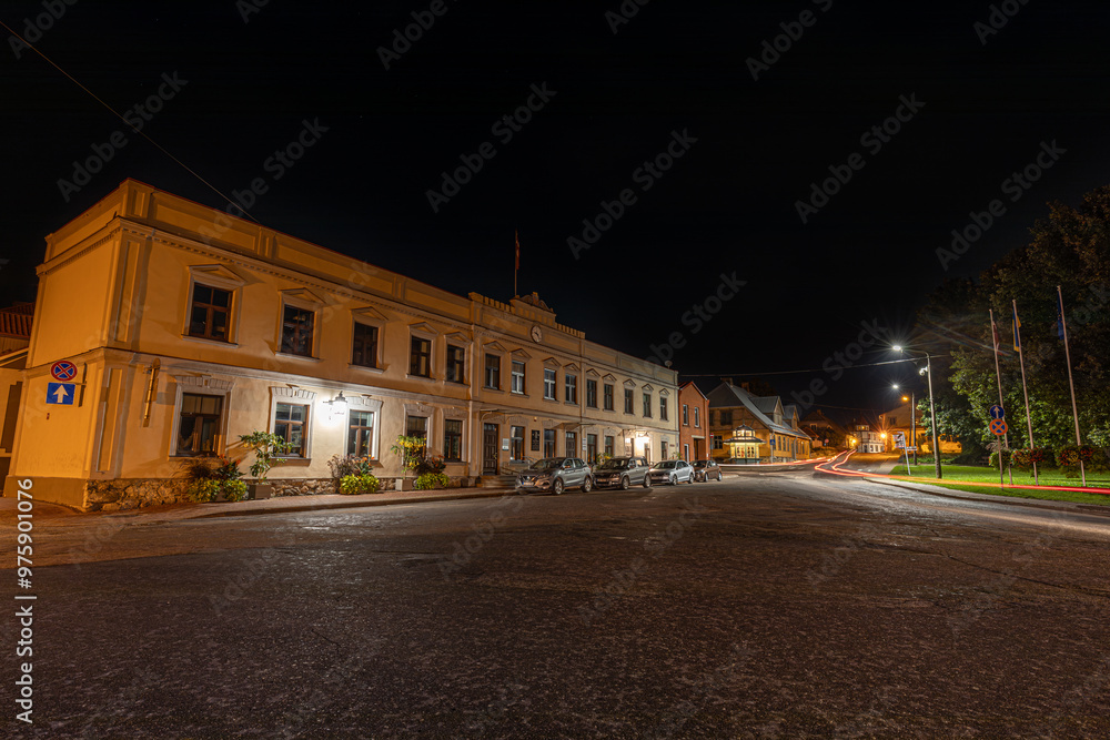 Fototapeta premium A peaceful night scene on a historic cobblestone street, illuminated by glowing streetlights that create star-shaped light flares. The warm glow of the lights highlights the charming architecture